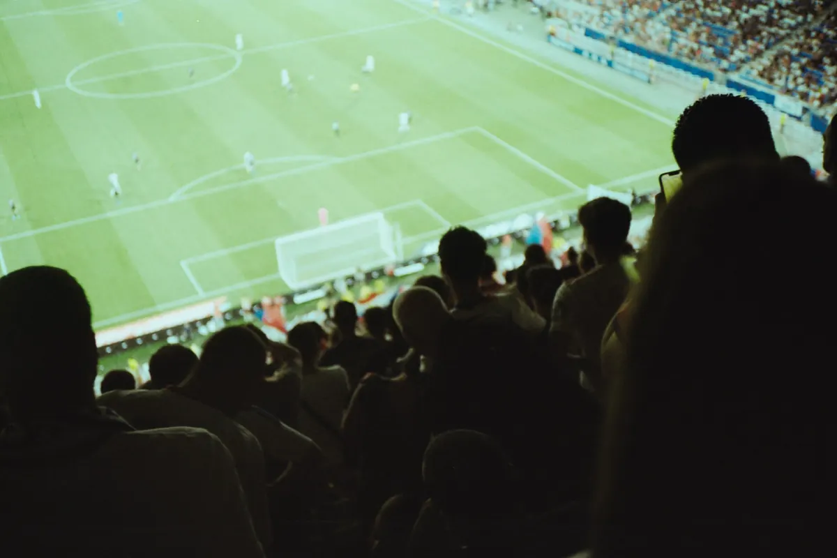 Hinchas de espaldas en la tribuna de un estadio mirando un partido de fútbol
